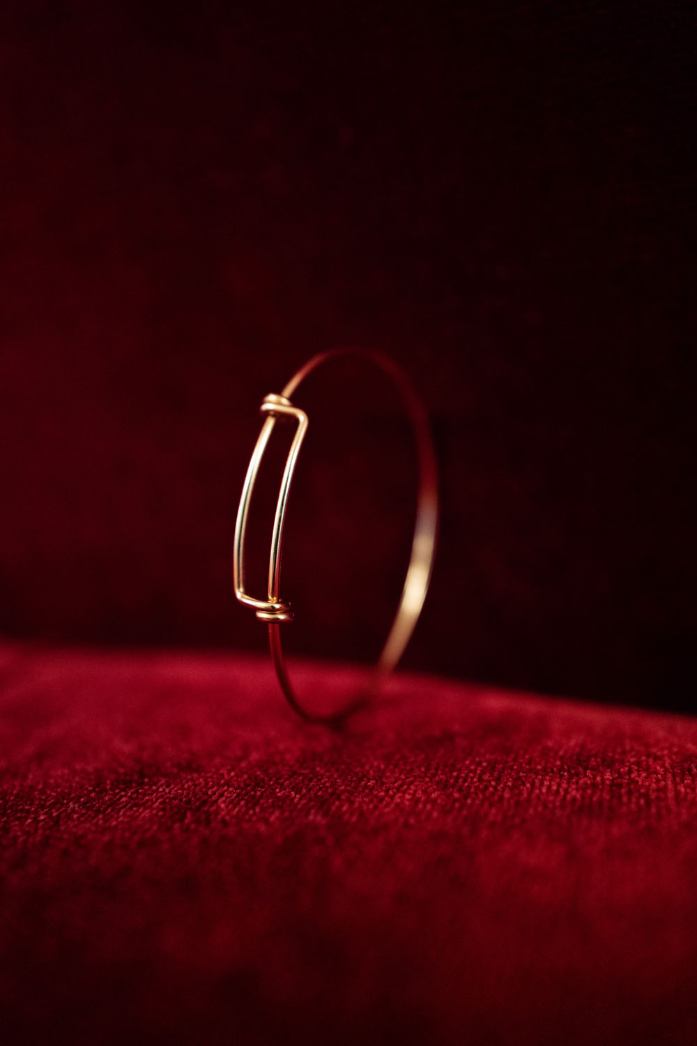 Bracelet fin en or au design minimaliste posé sur un tissu en velours rouge.