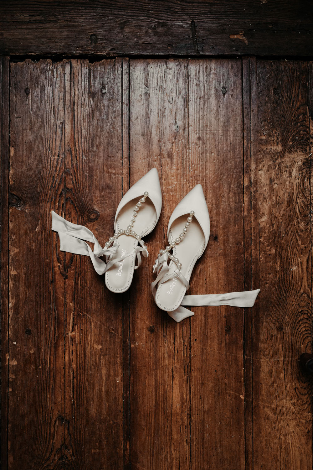 Paire de chaussures de mariée blanches à talons posées sur un sol en bois rustique.