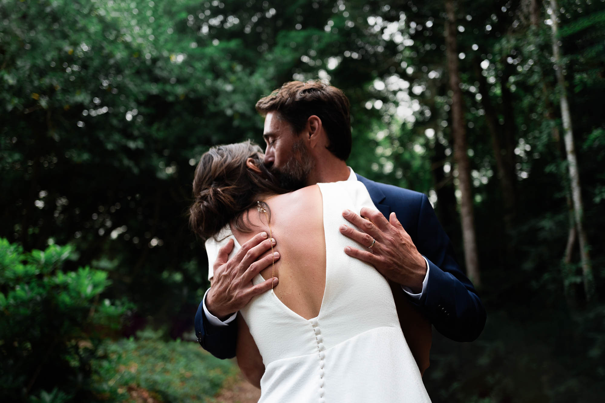 Couple de mariés s’enlaçant tendrement dans un cadre boisé, la mariée en robe blanche.