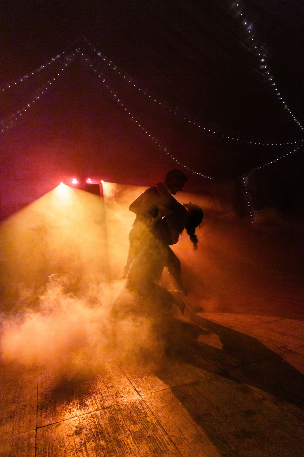 Couple de mariés effectuant une danse élégante entouré de lumière et de fumée lors de leur réception de mariage.