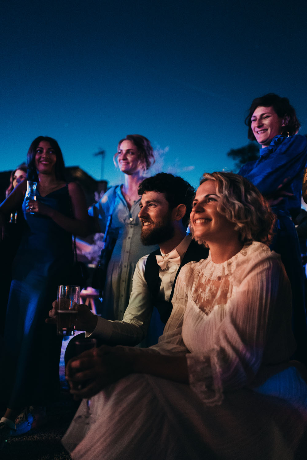 Groupe d’invités lors d’une soirée de mariage en extérieur, vêtus élégamment sous un ciel nocturne.
