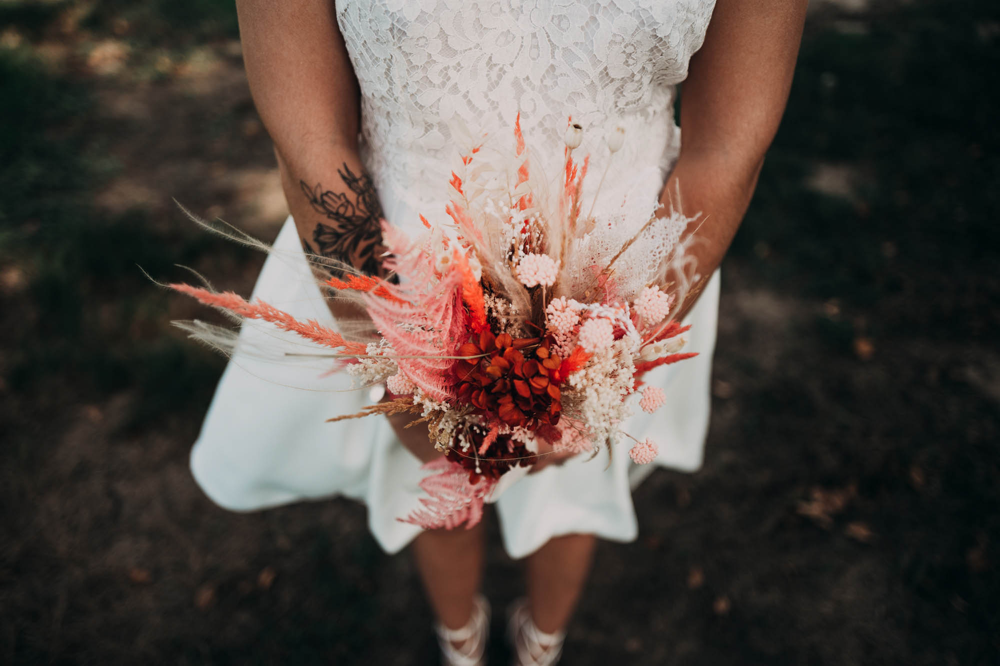 Mariée en robe blanche tenant un bouquet de fleurs séchées lors d’un mariage champêtre en extérieur.