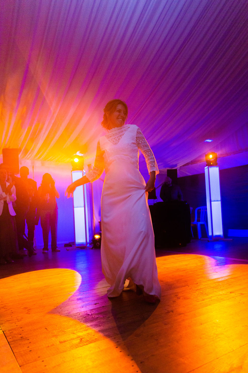 Mariée en robe blanche dansant sur la piste éclairée lors de la réception de mariage sous une tente.