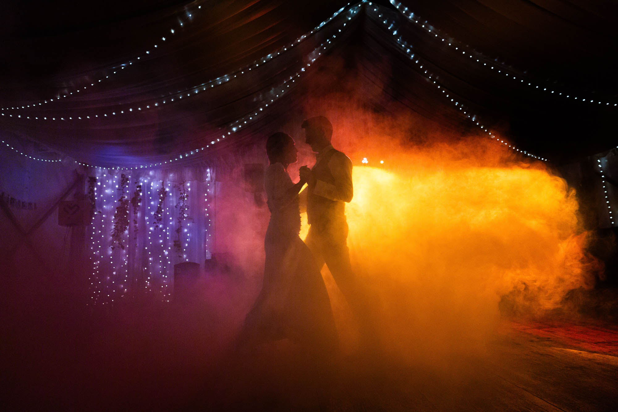 Silhouette d’un couple de mariés dansant entouré de lumières et de fumée lors de leur soirée de mariage.