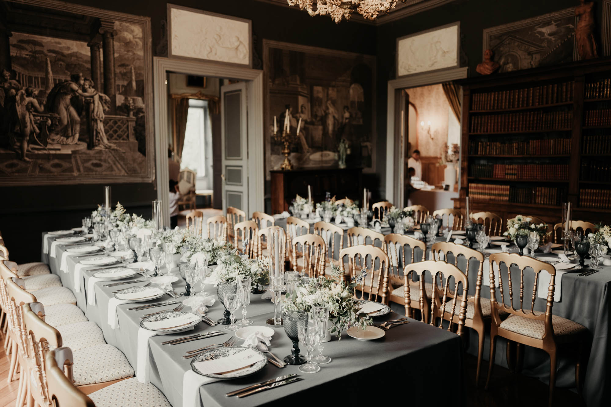 Tables de réception élégamment dressées pour un mariage dans une salle château avec livres anciens et décor raffiné.